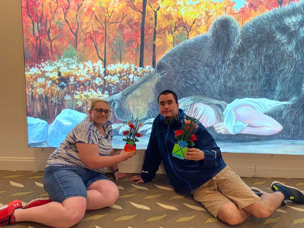 People holding flowers in front of painting of bear and girl