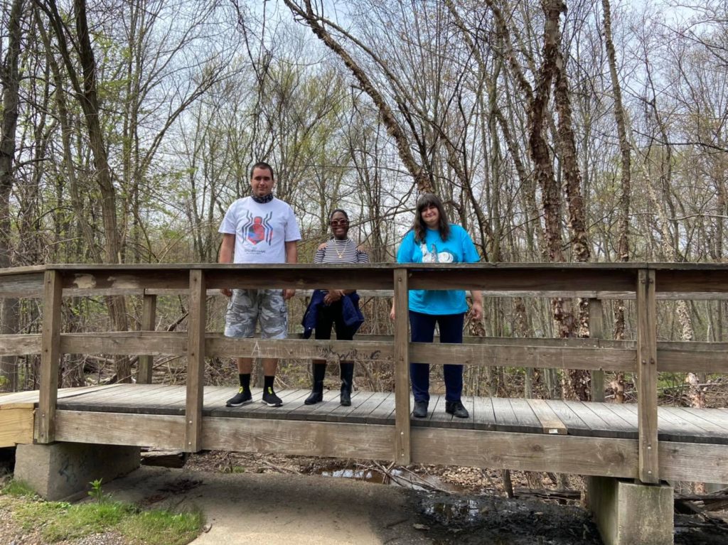 People standing on wooden bridge above small creek